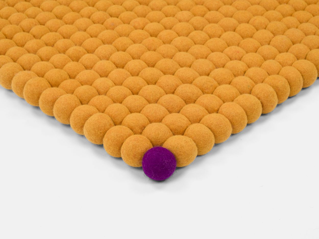 Detailaufnahme: Ockergelber Filzteppich "Big One" mit Filzkugeln, 180x260 cm, ein lila Detail.