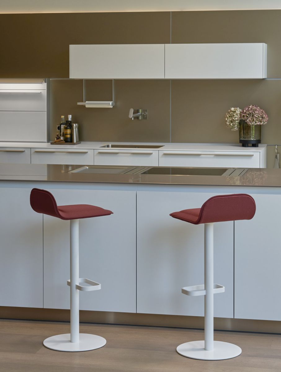 Zwei weiße Barhocker mit weinroten Sitzpolstern der Marke Moree vor einer Küchenzeile.