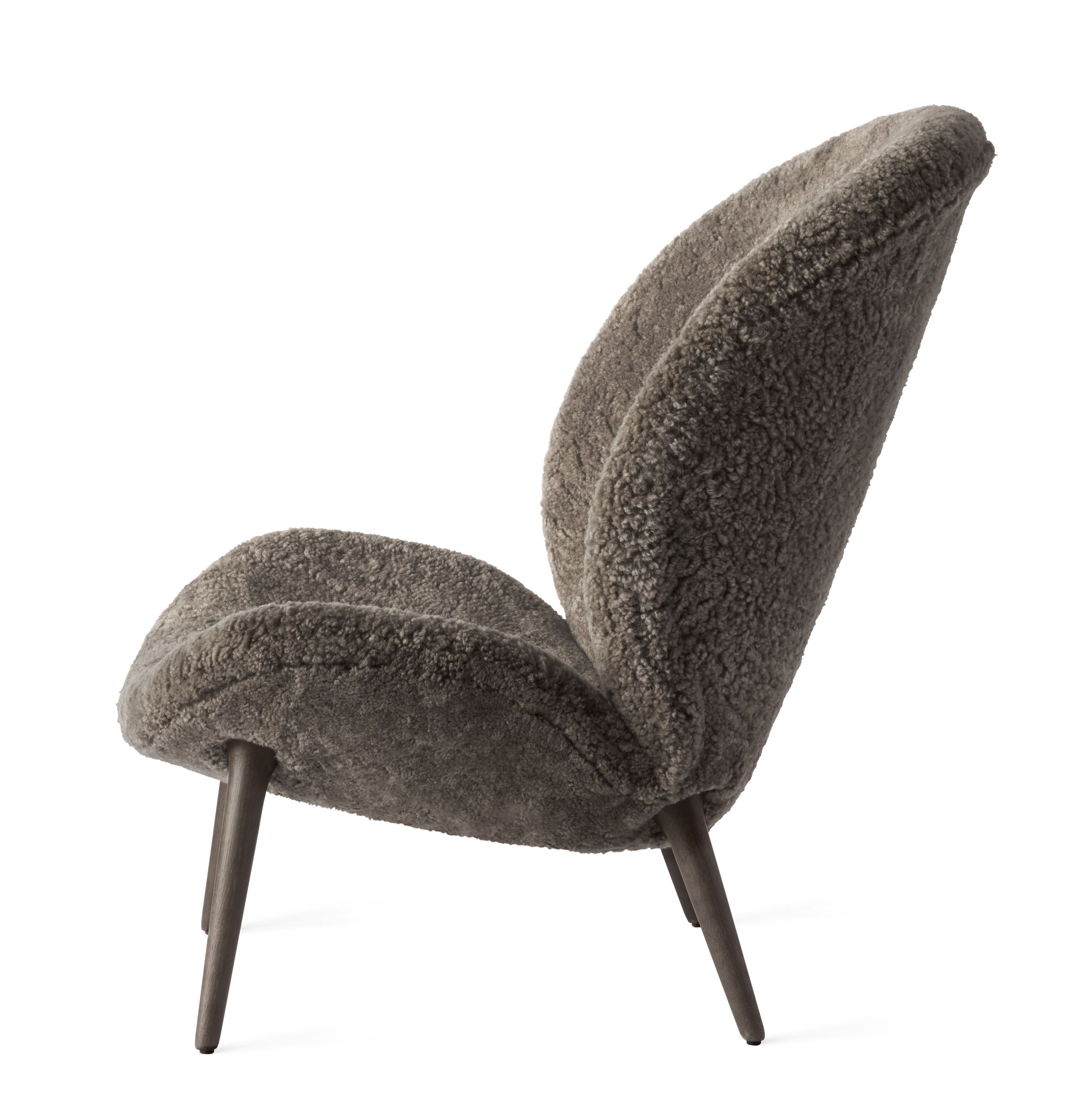 Lodge Loungestuhl von Vipp, seitliche Ansicht. Gemütlicher Sessel mit grauem Schaffell und Holzfüßen.