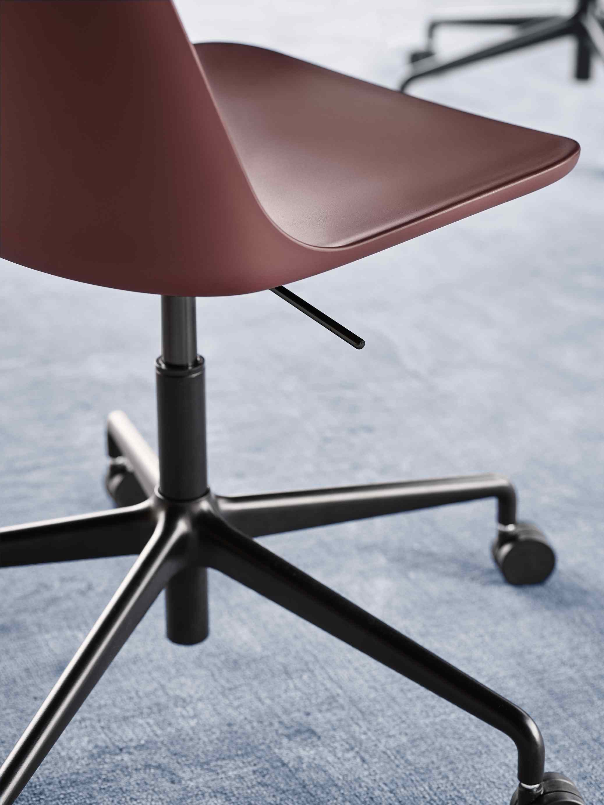 Detailaufnahme des Rely Drehstuhls von AndTradition in Bordeauxrot mit schwarzem Fußkreuz und Rollen.