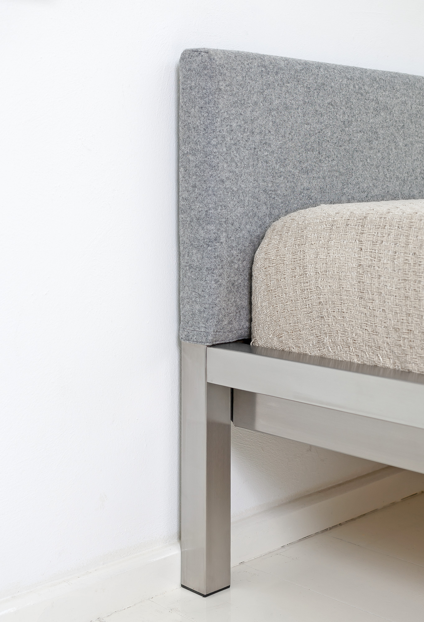 Detailaufnahme: Pure Bett mit Edelstahlrahmen und grauem Velito Polsterkopfteil von Hans Hansen.