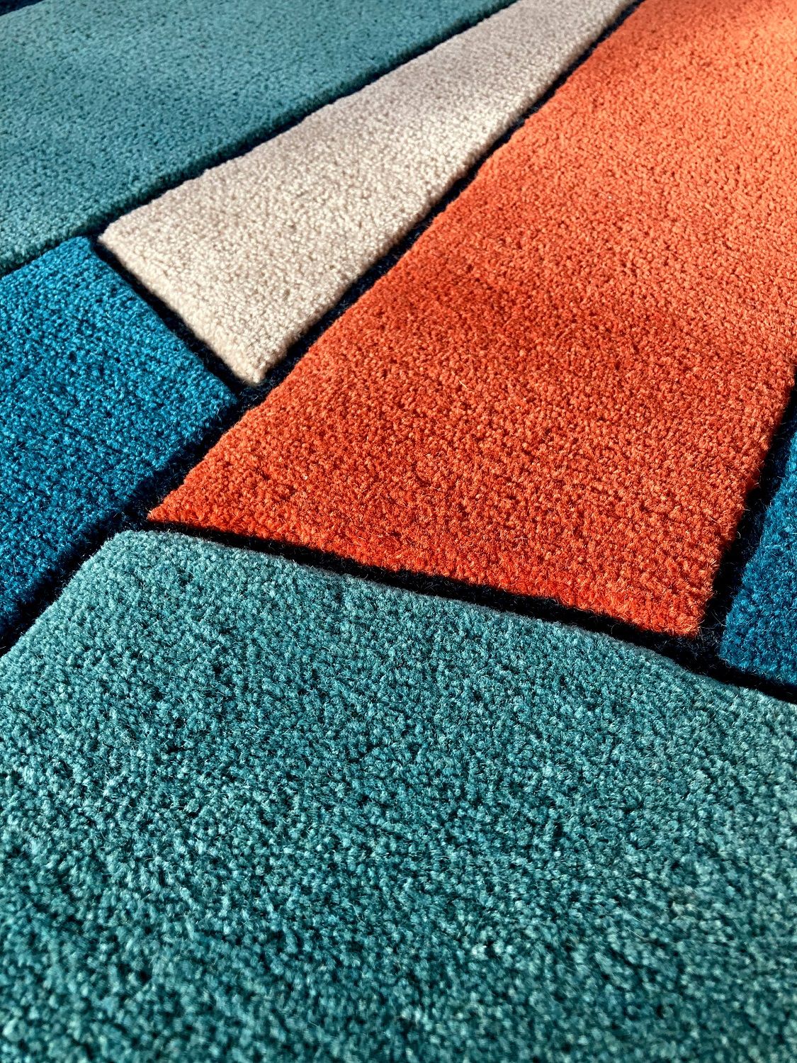 Detailaufnahme des Inès Carpet Teppichs von Hartô mit geometrischem Muster in Blau, Orange und Beige.
