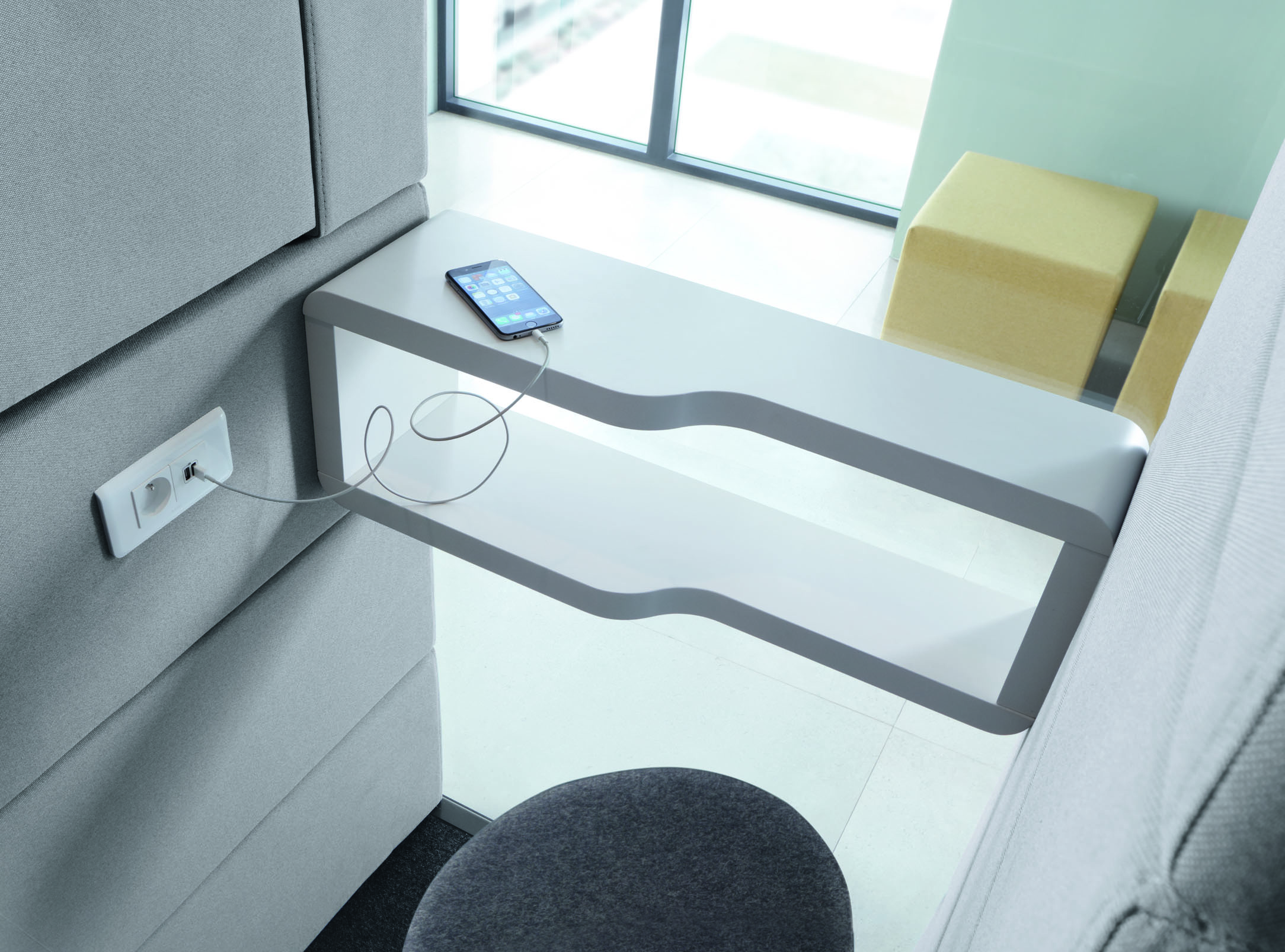 Modernes Büro: Graue Akustikkabine mit weißem Tisch, Handy am Ladekabel an der Wand.