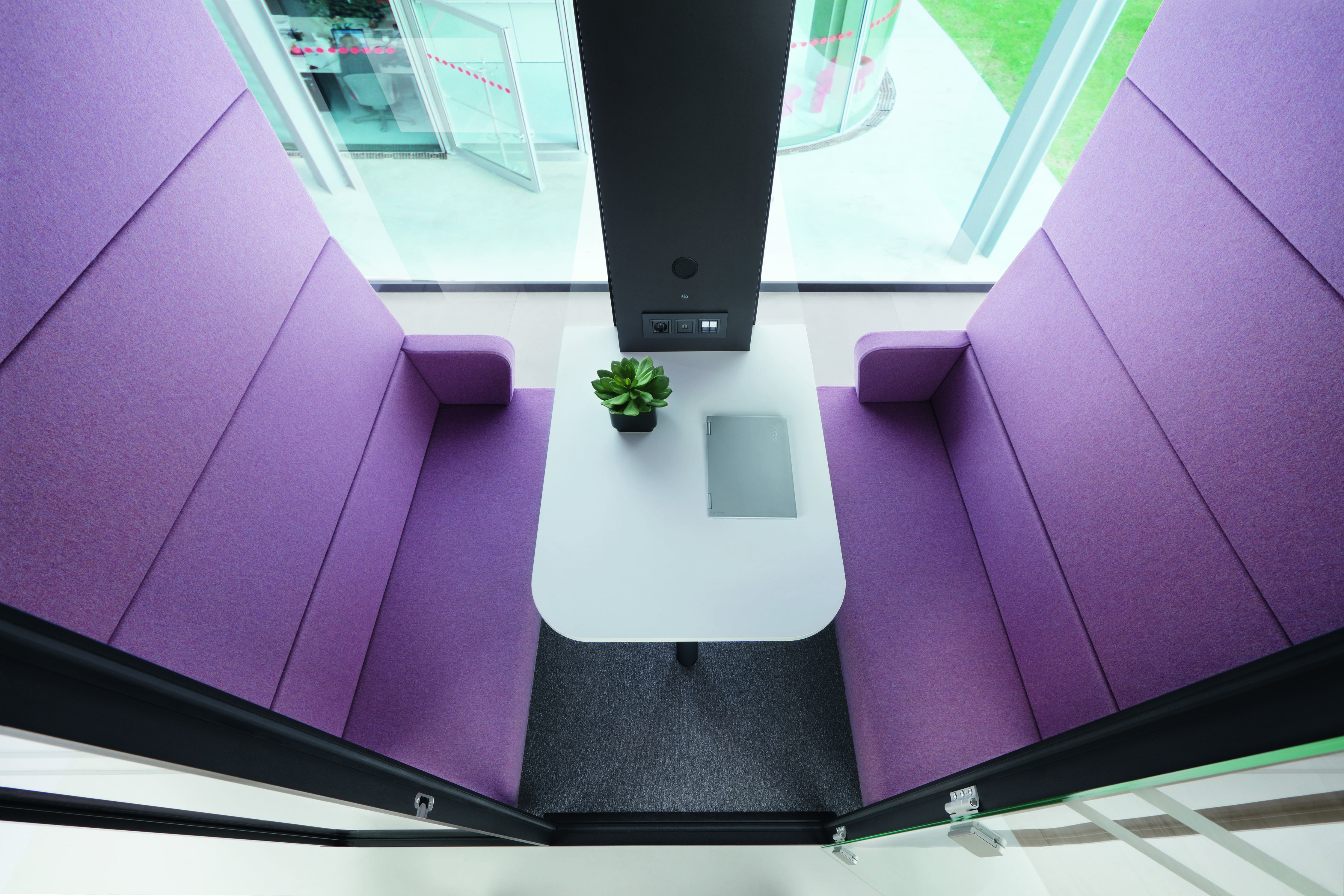 HushMeet Meetingbox: Innenansicht mit lila Sitzelementen, weißem Tisch und Laptop. Büro Besprechungsraum.