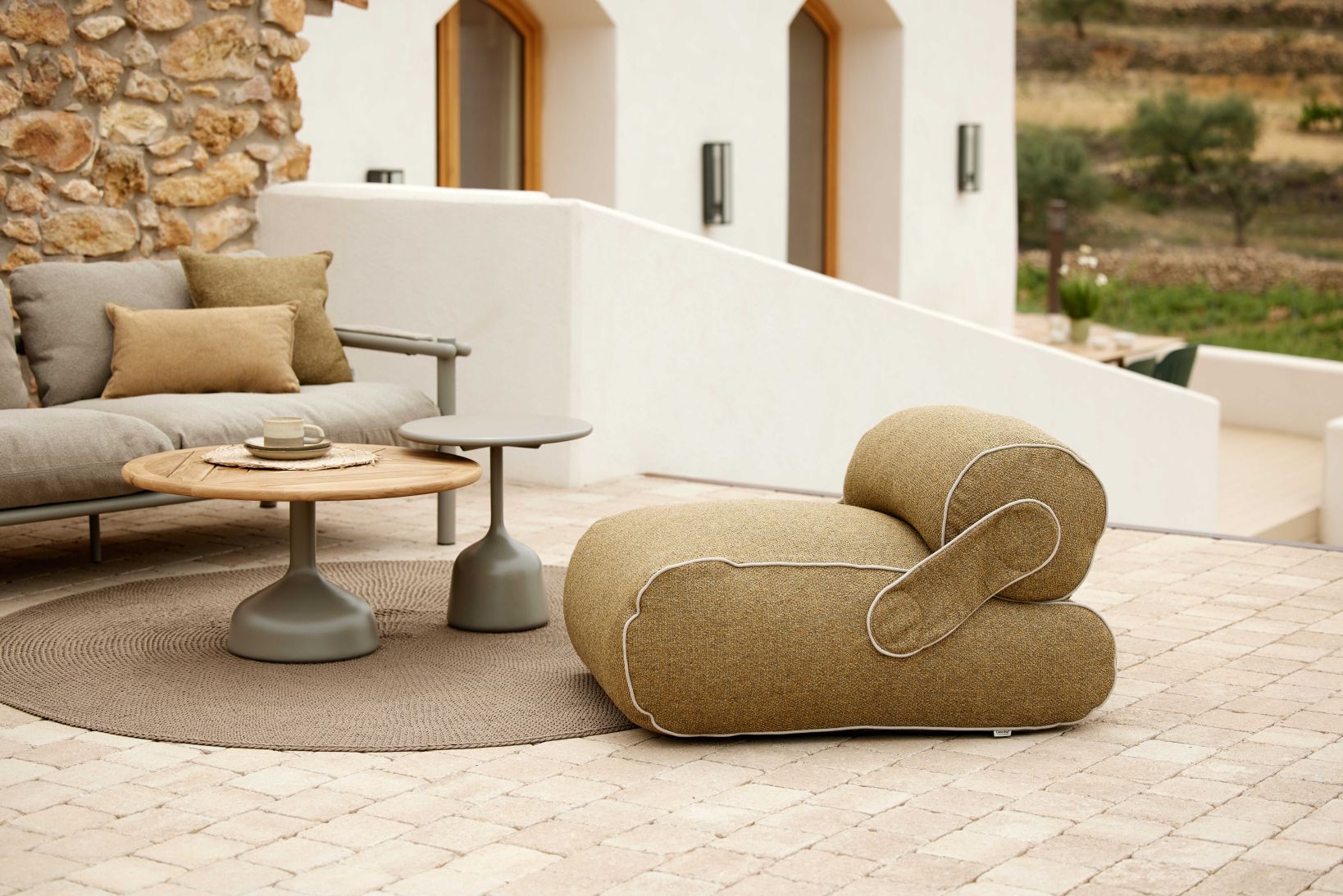 Unite Loungesessel von Cane-Line in Beige, Teil einer Outdoor-Lounge mit Sofa und Beistelltischen.