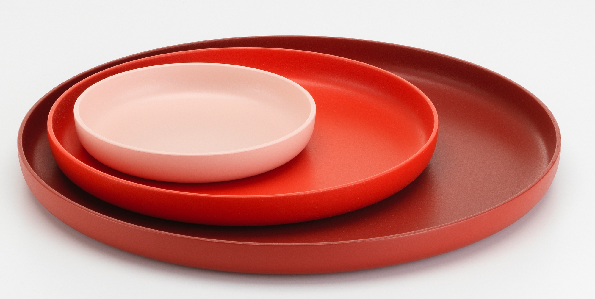 Vitra Trays Tablett-Set: Drei runde Tabletts in Rot- und Rosatönen gestapelt, modernes Design für Wohnaccessoires.