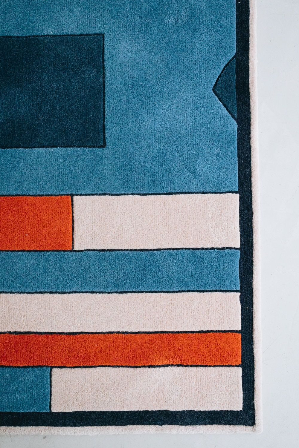 Detailaufnahme des Hartô Teppichs Inès mit blauem, orangefarbenem und weißem geometrischen Muster.