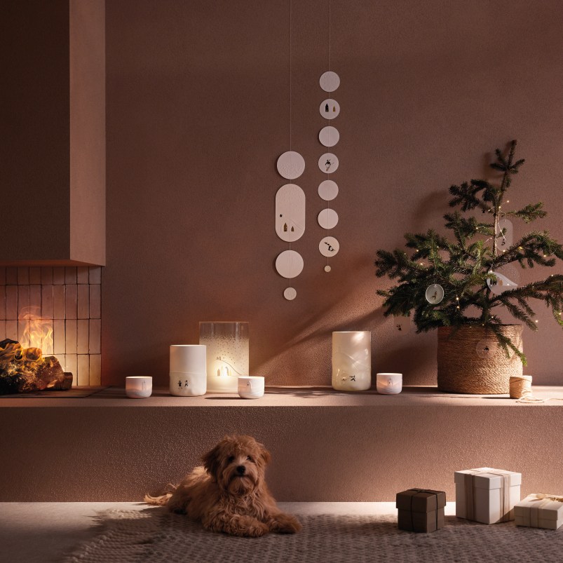 Winterliche Dekoration mit Poesie Windlicht, Schneelandschaft-Motiven, kleinem Weihnachtsbaum, Geschenken und Hund vor Kamin.