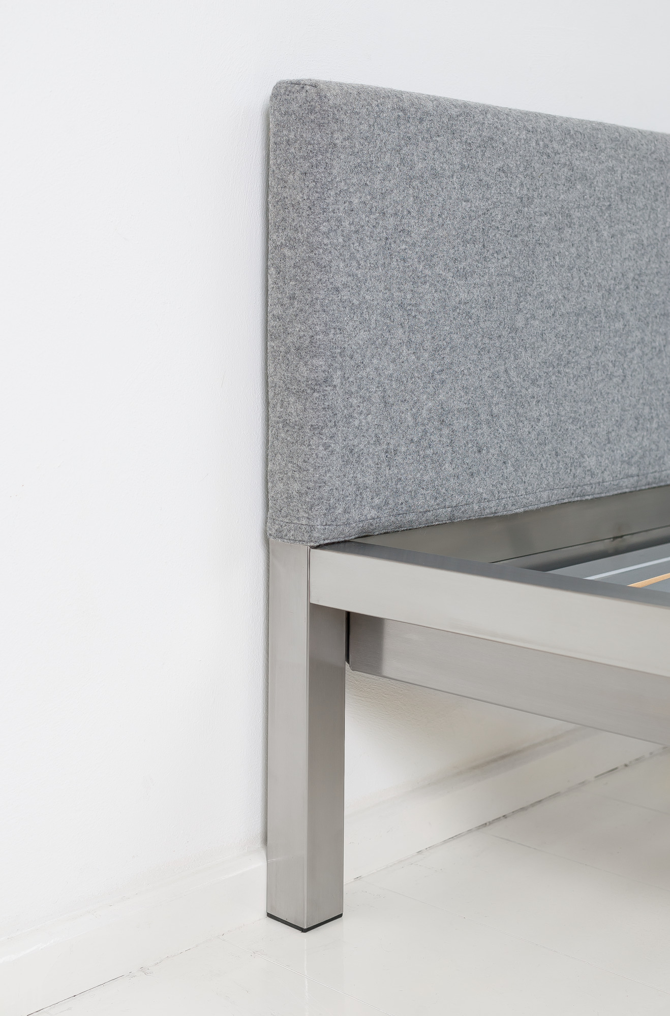 Detailaufnahme: Pure Bett mit Edelstahlrahmen und grauem Velito Polsterkopfteil von Hans Hansen.