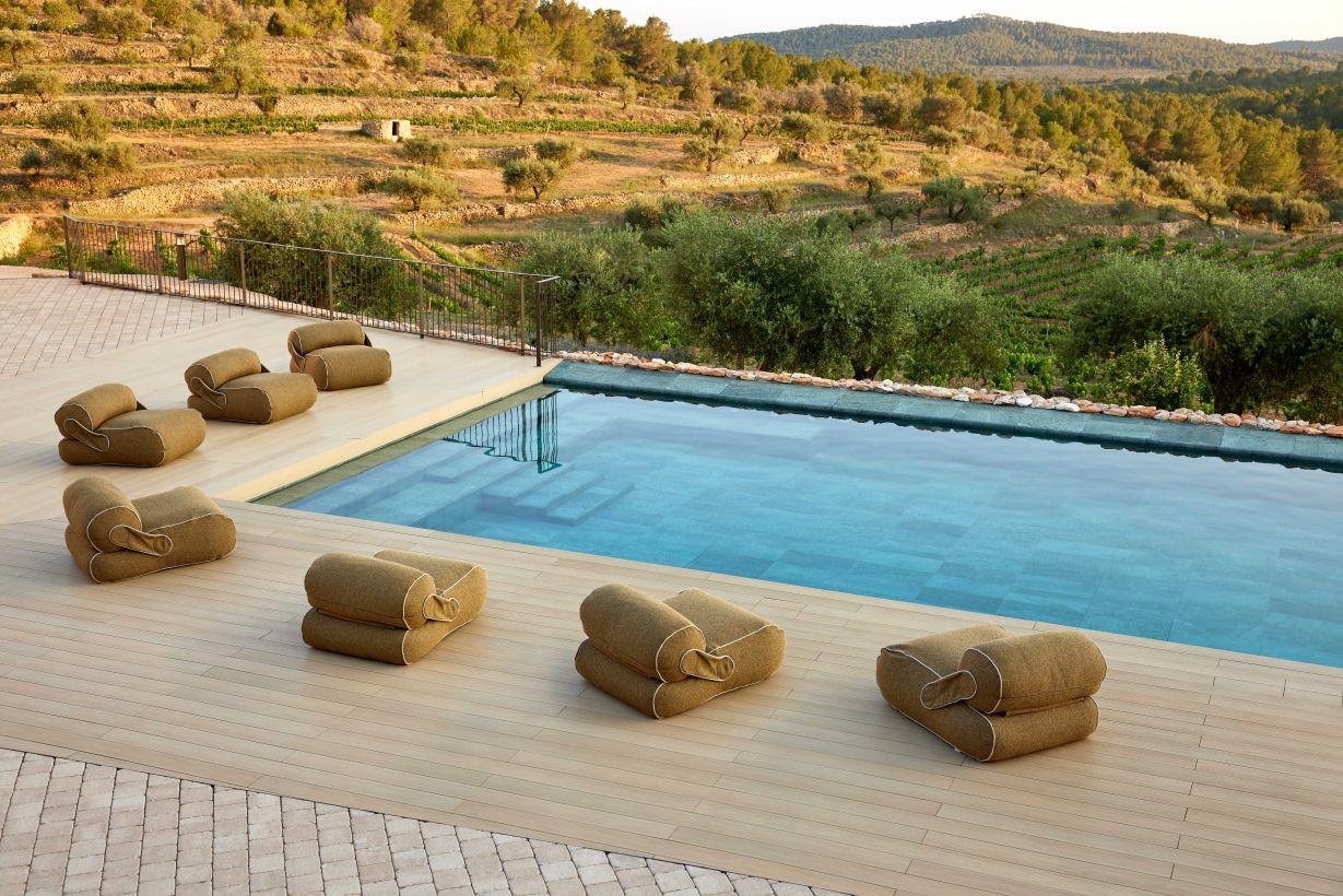 Cane-Line Unite Outdoor Loungesessel aus Stoff in Beige am Pool mit Blick auf die Landschaft.
