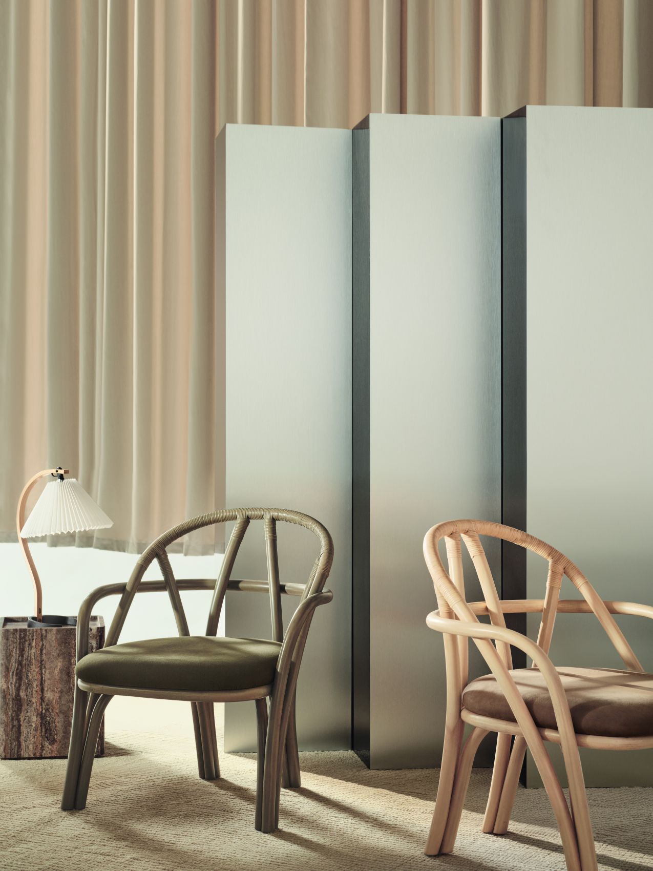 Nahaufnahme der Gubi Timberline Tischleuchte auf einem Holzhocker, neben zwei Rattanstühlen in einem stilvollen Interieur.