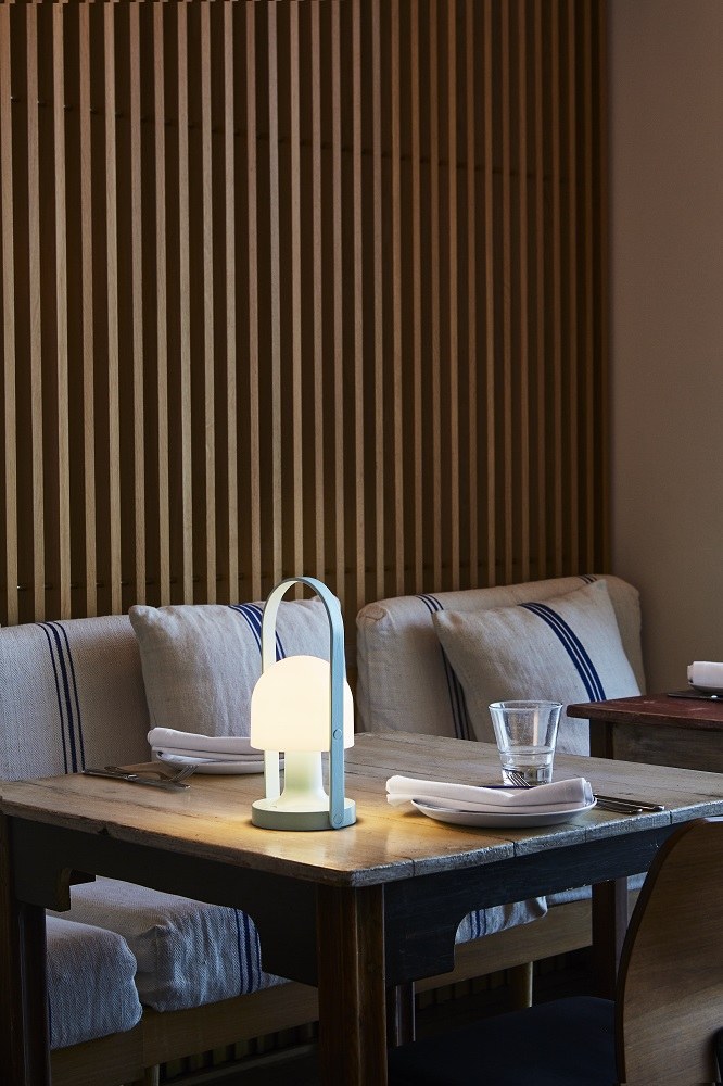 FollowMe LED Akkuleuchte von Marset auf gedecktem Tisch im Restaurant, warmes Licht.