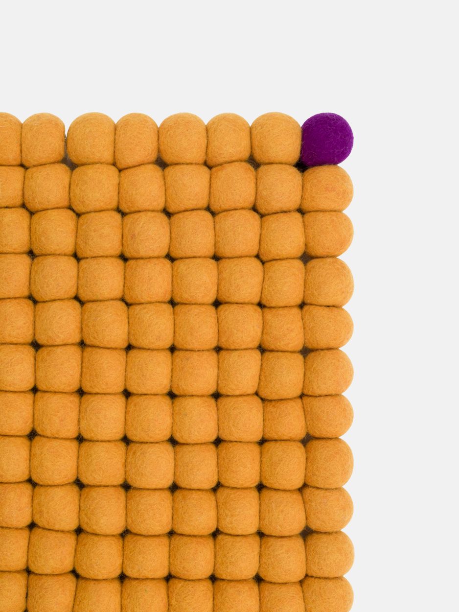 Detailaufnahme: Ockergelber Filzteppich aus Filzkugeln, ein lila Akzent. myfelt Teppich, rechteckig.
