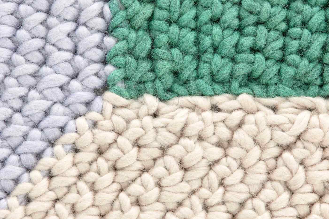 Detailaufnahme des The Crochet Collection Teppichs in Blau, gehäkelt mit dicken Wollfäden in Grau, Grün und Beige.