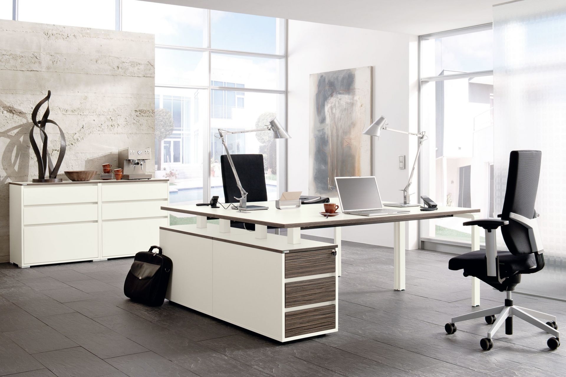 Moderner Büroraum mit Palmberg Pensum Besprechungstisch in Ellipsenform, Bürostuhl, Schreibtischlampe und Laptop.