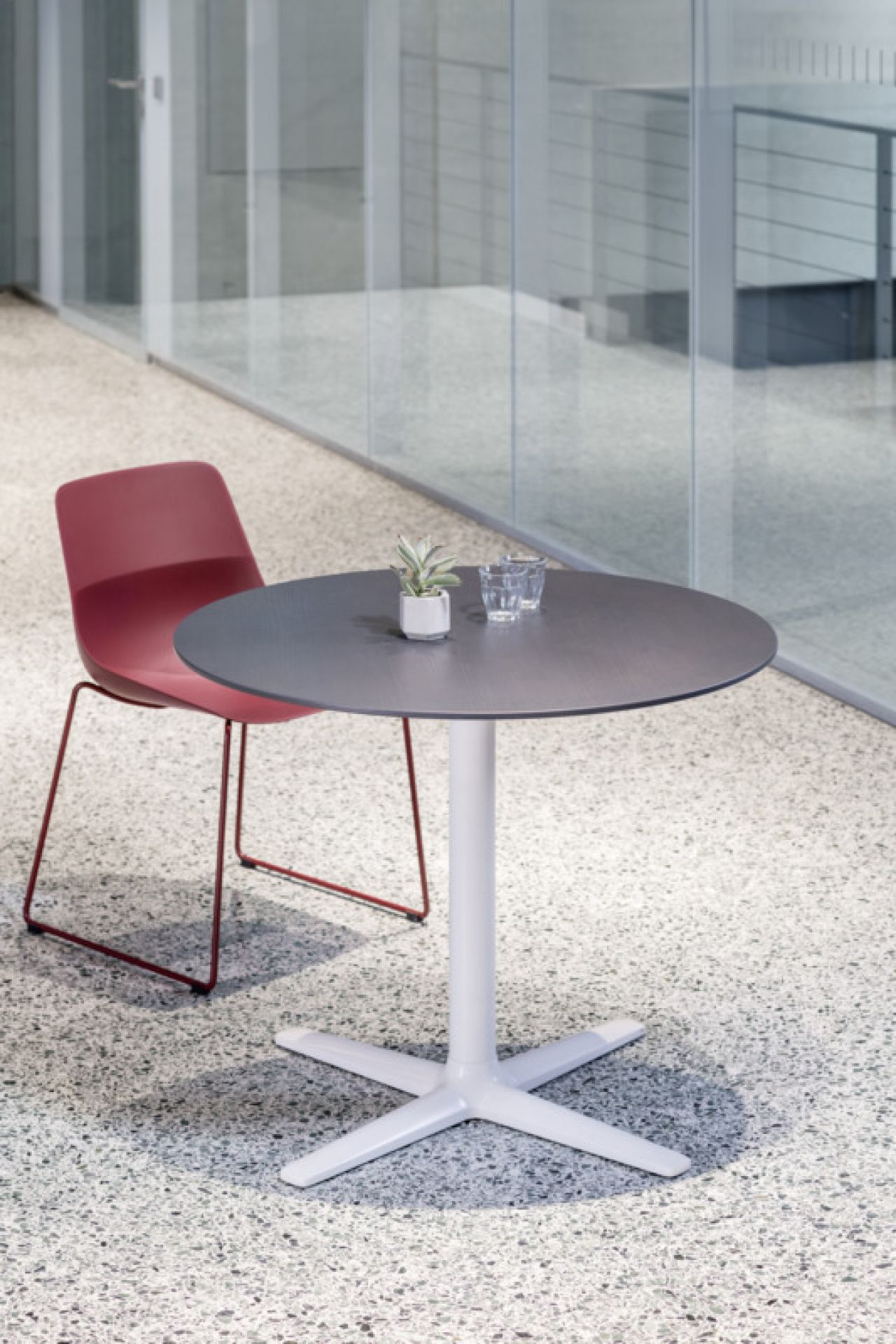 Roter Brunner Crona Light Kufenstuhl neben rundem Tisch mit weißem Fuß im Büro.