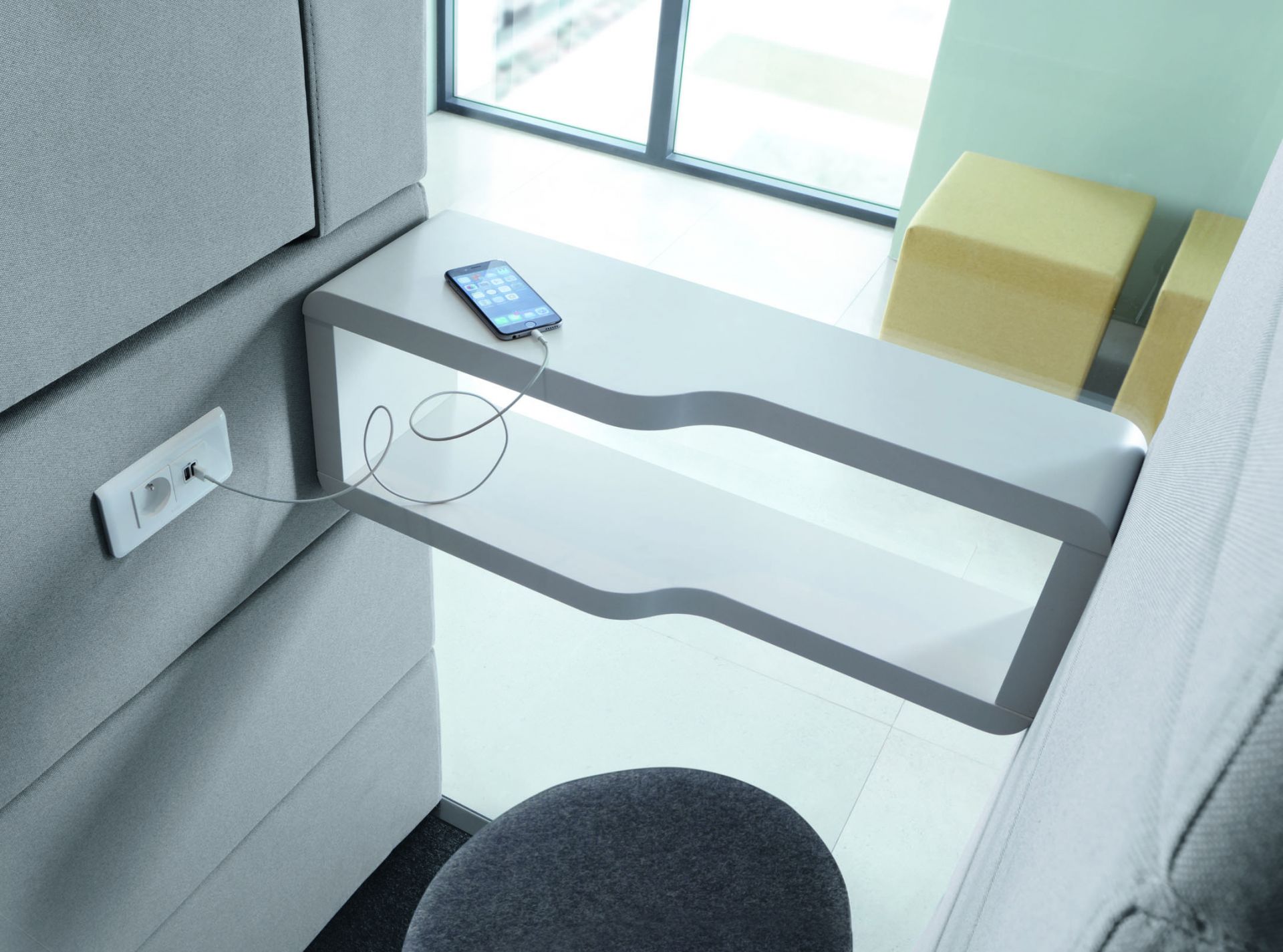 Modernes Büro: Graue Akustikkabine mit weißem Tisch, Handy am Ladekabel an der Wand.