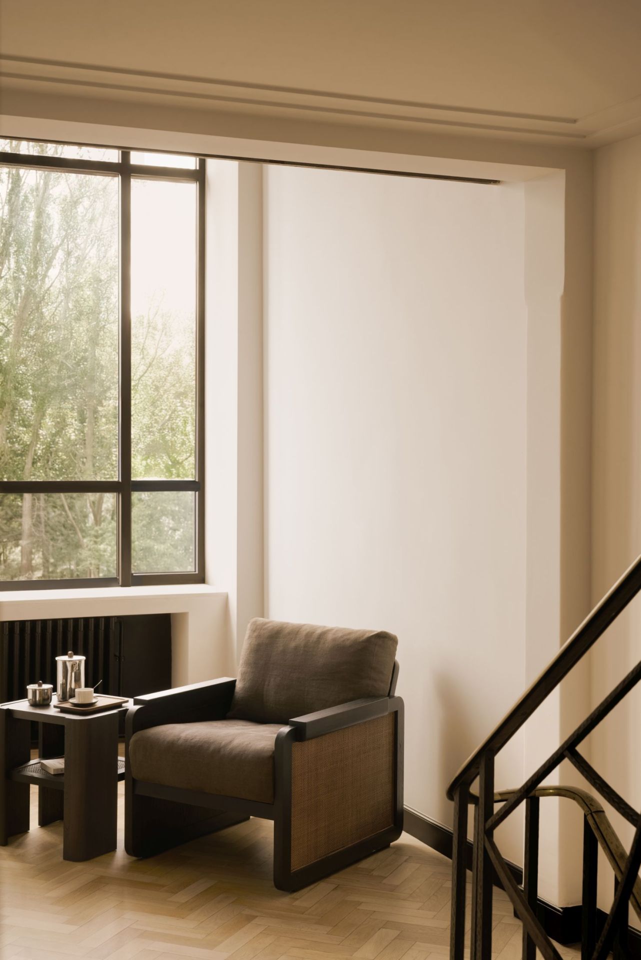 Ethnicraft Panel Beistelltisch aus dunklem Holz neben Sessel mit Getränken im hellen Raum.