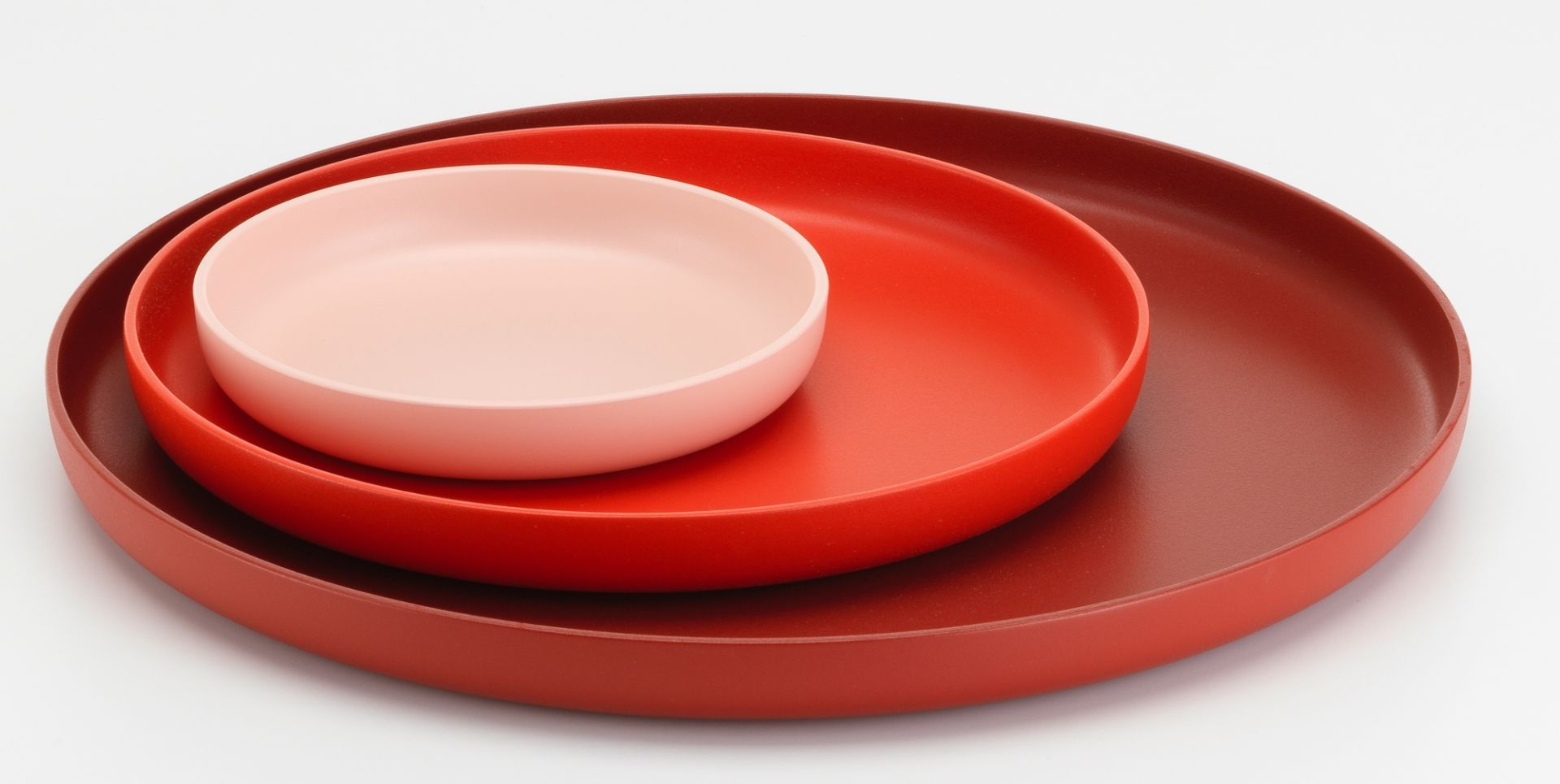 Vitra Trays Tablett-Set: Drei runde Tabletts in Rot- und Rosatönen gestapelt, modernes Design für Wohnaccessoires.