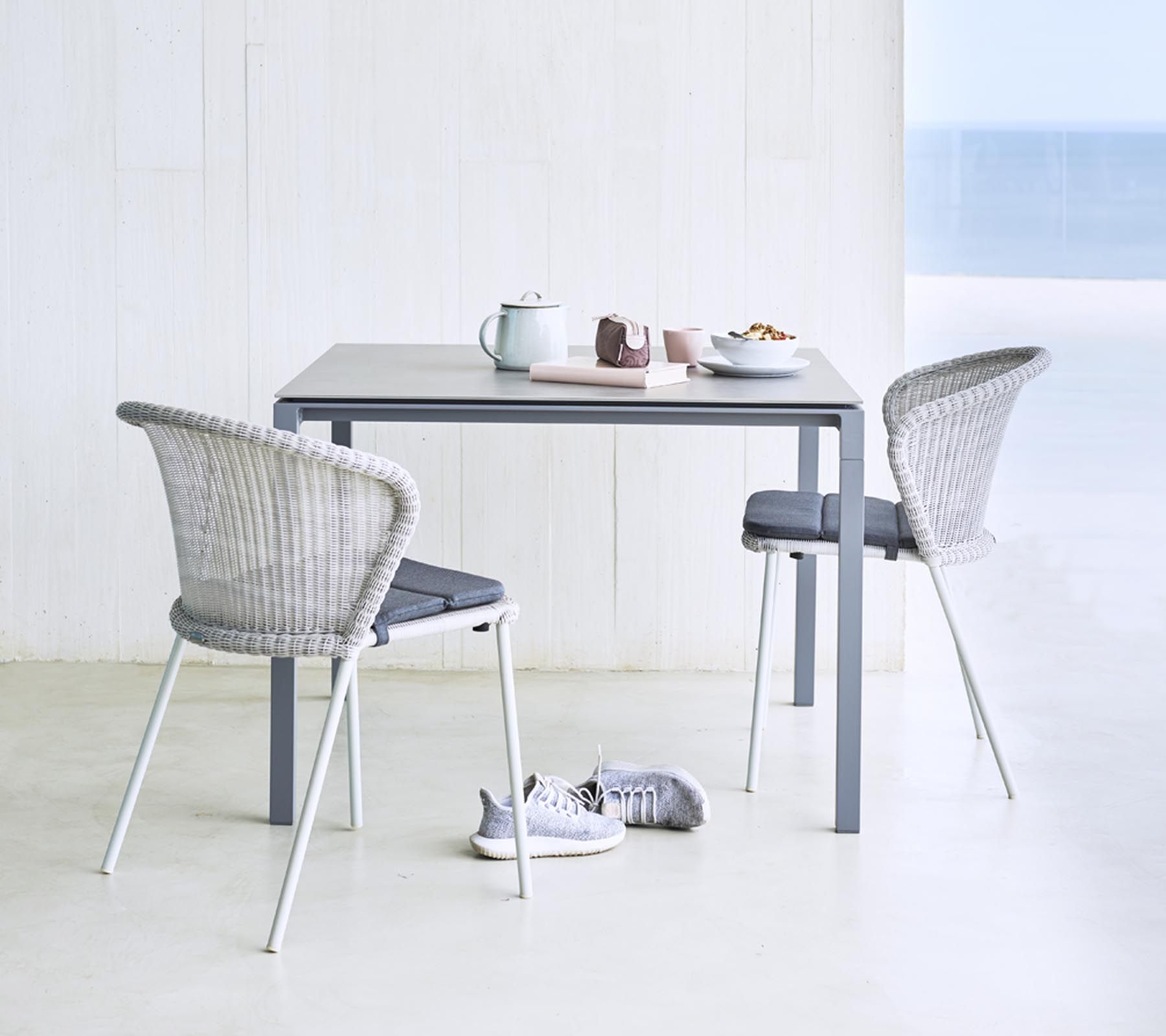 Lean Stuhl von Cane-Line, weiße Rattan-Optik mit grauem Kissen, für Garten und Terrasse.