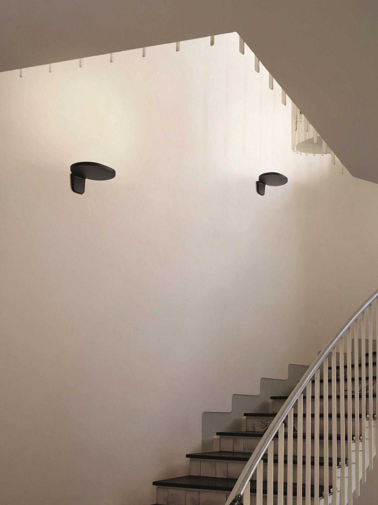 Zwei schwarze Oplight W1 Wandleuchten von Flos an einer Treppenhauswand, modernes Design.