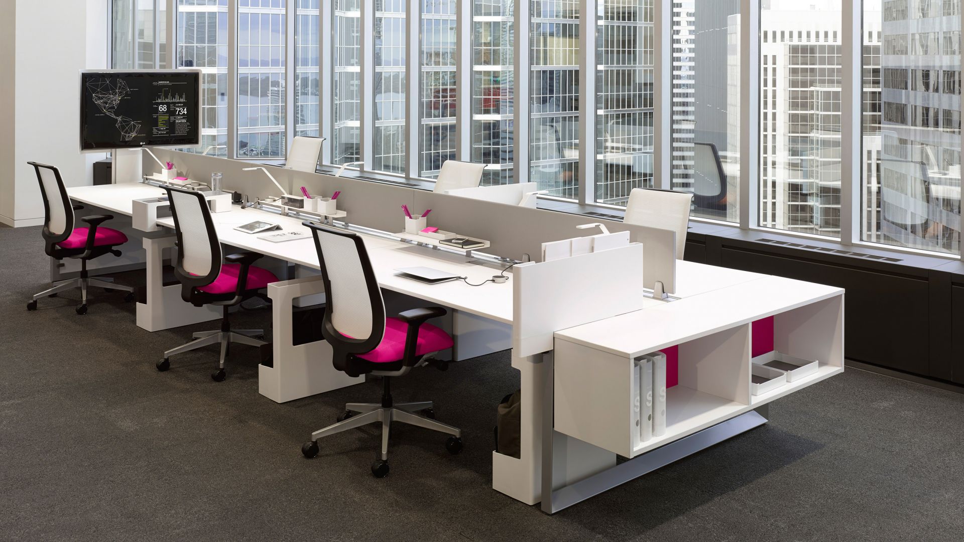 Büroarbeitsplatz mit weißen Schreibtischen und Steelcase Reply Bürostühlen mit Netzrücken und pinkfarbener Sitzfläche.