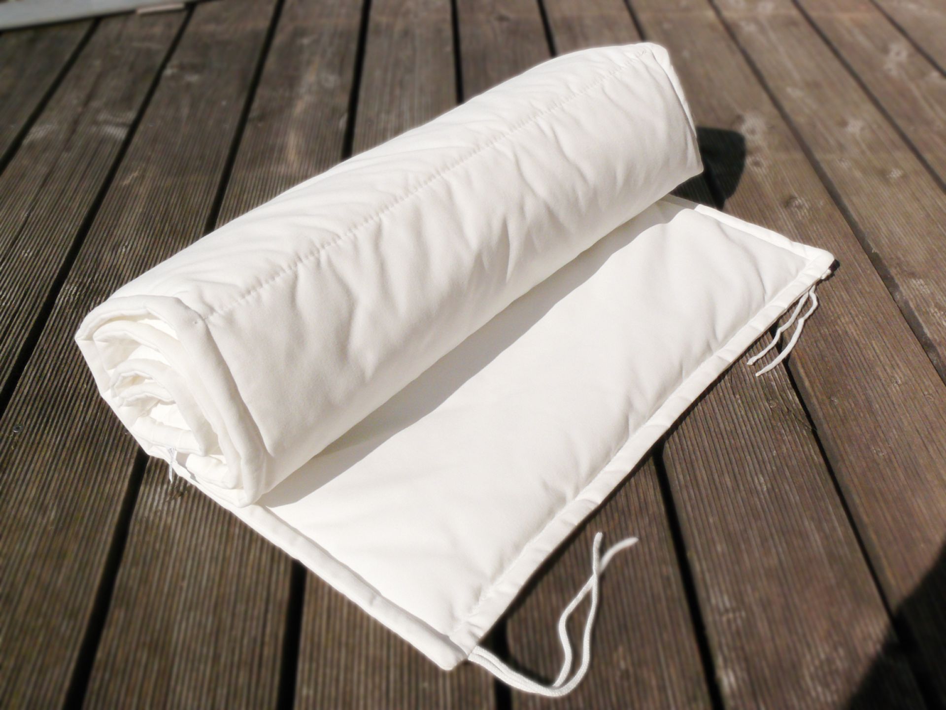 Aufgerollte, weiße Luxury Auflage von Jan Kurtz auf einer Holzterrasse. Bequeme Sitzauflage für Gartenmöbel.