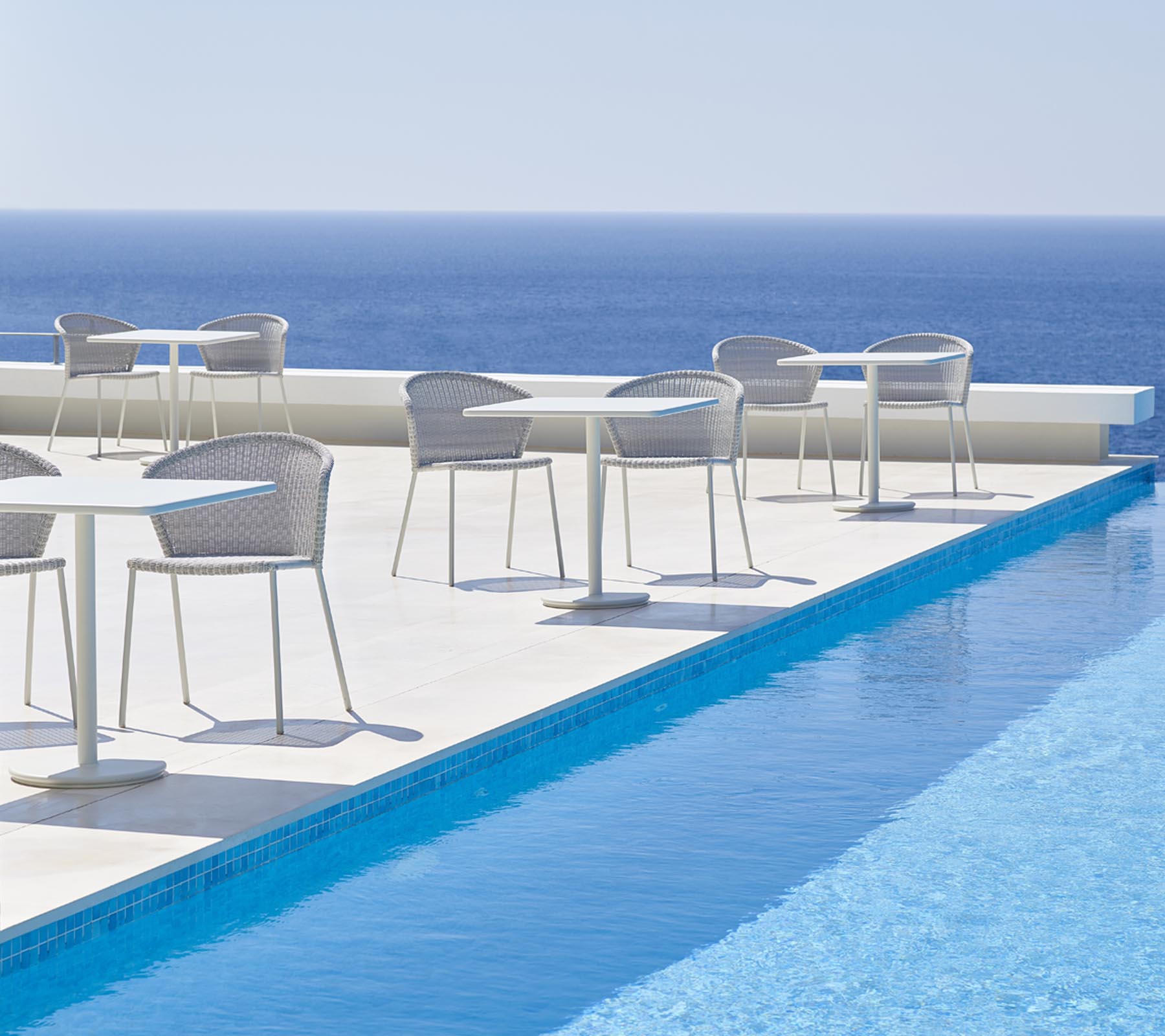 Lean Stuhl von Cane-Line, weiß, mit grauem Kissen, Outdoor Möbel am Pool.